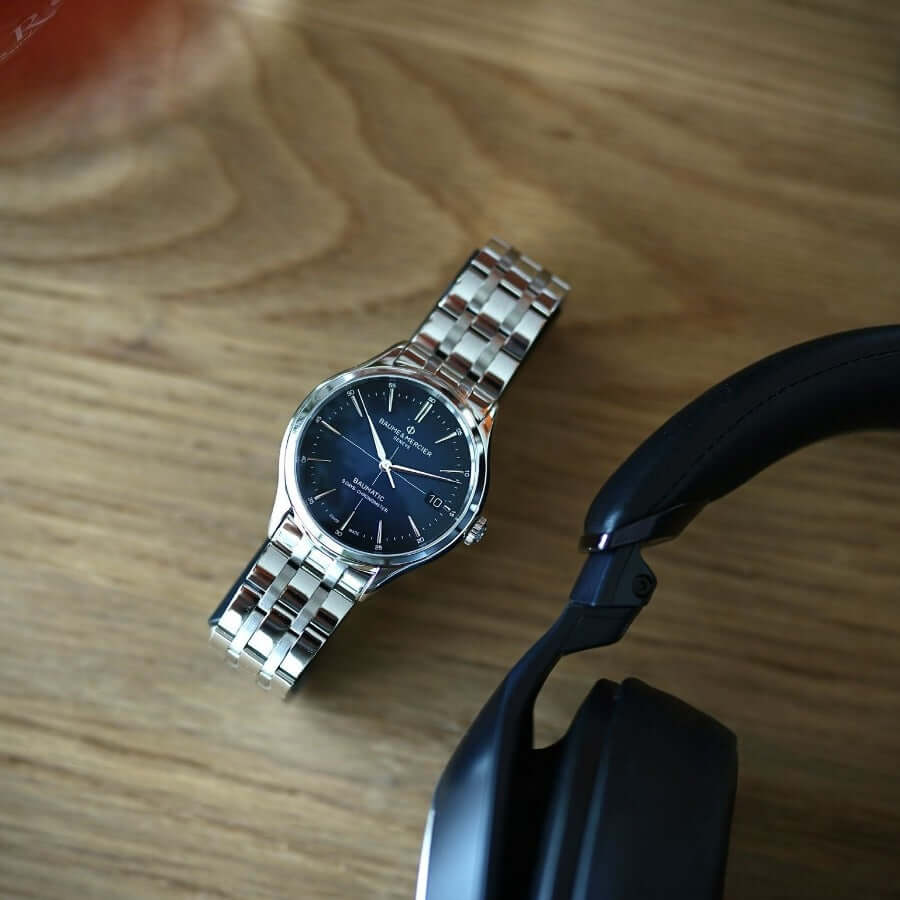 Baume & Mercier Clifton Baumatic 10468 -kello metallirannekkeella, tummalla taululla ja langattomalla kuulokkeella.