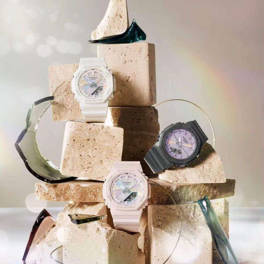 Casio G-Shock Rannekello GMA-P2100PC-4AER kolme kelloa, vaaleat ja tummat mallit, asetettu kiviesineelle.