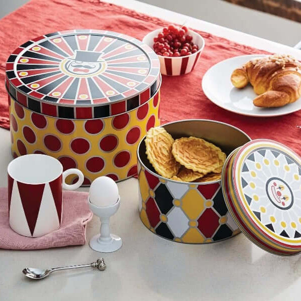 Alessi Circus säilytysrasiat MW31S3 värikkäillä kuvioinneilla pöydällä, sisältäen keksejä ja aamiaistarvikkeita.