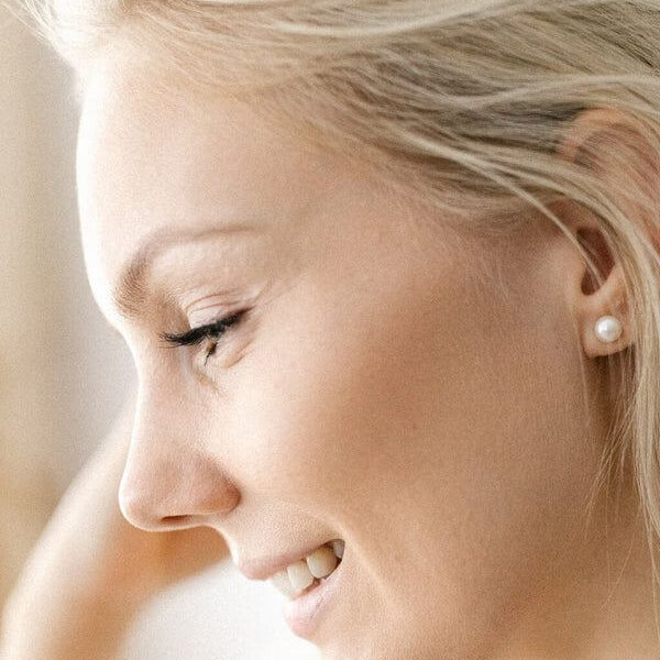 Gaura Pearls Ellen helmikorvakorut EFB04W päällä olevalla naisella, joka hymyilee ja katsoo sivulle.