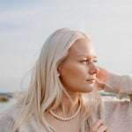 Nuori nainen katsoo horisonttiin Gaura Pearls helminauha FARW685 kaulallaan.