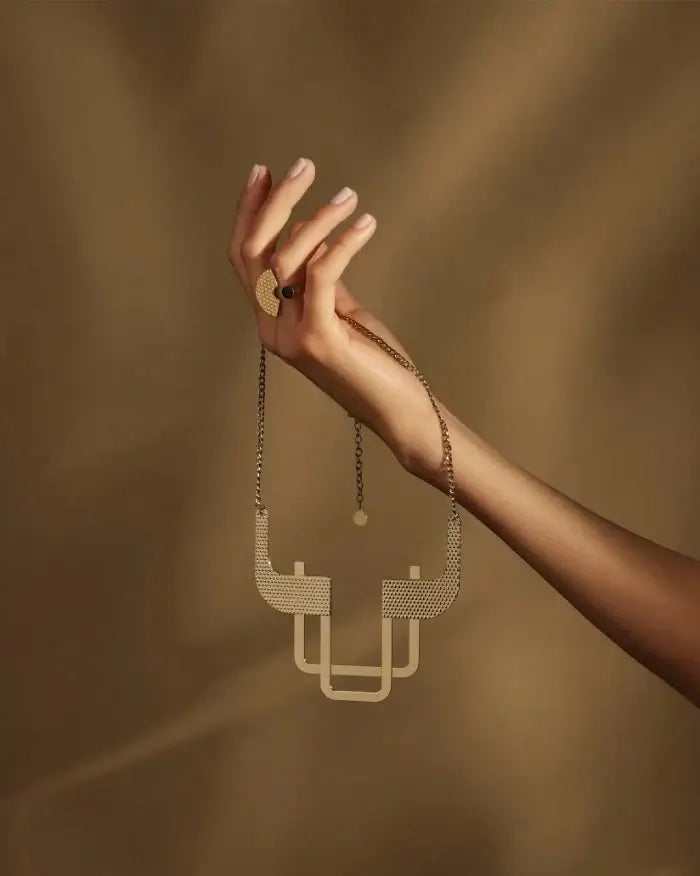 Alessi Trama Kaulakoru ESA014 elegantti kaulakoru pidettynä kädessä, jossa on moderni muotoilu.